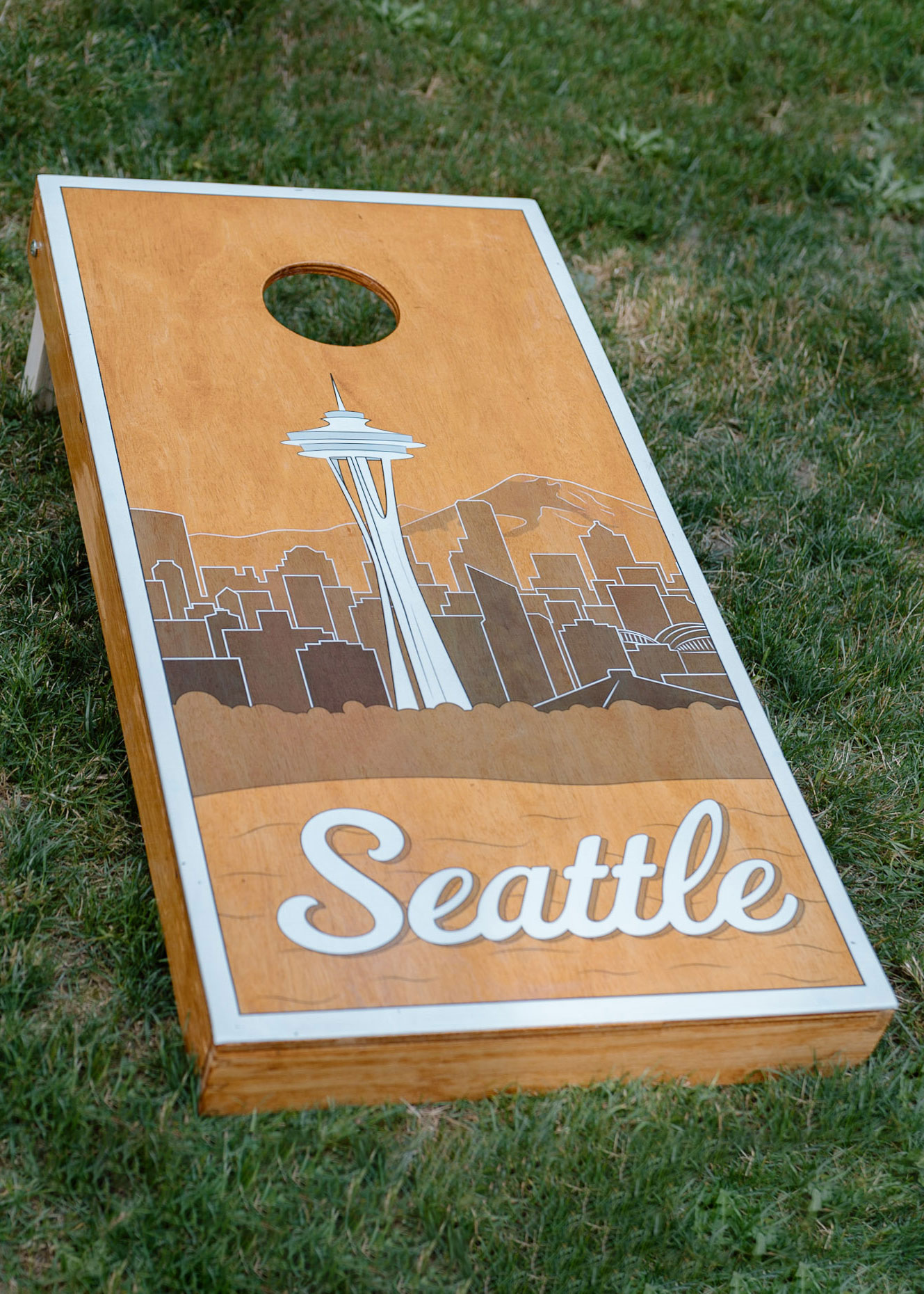 A custom cornhole board with an illustrated and stylized skyline of Seattle.  