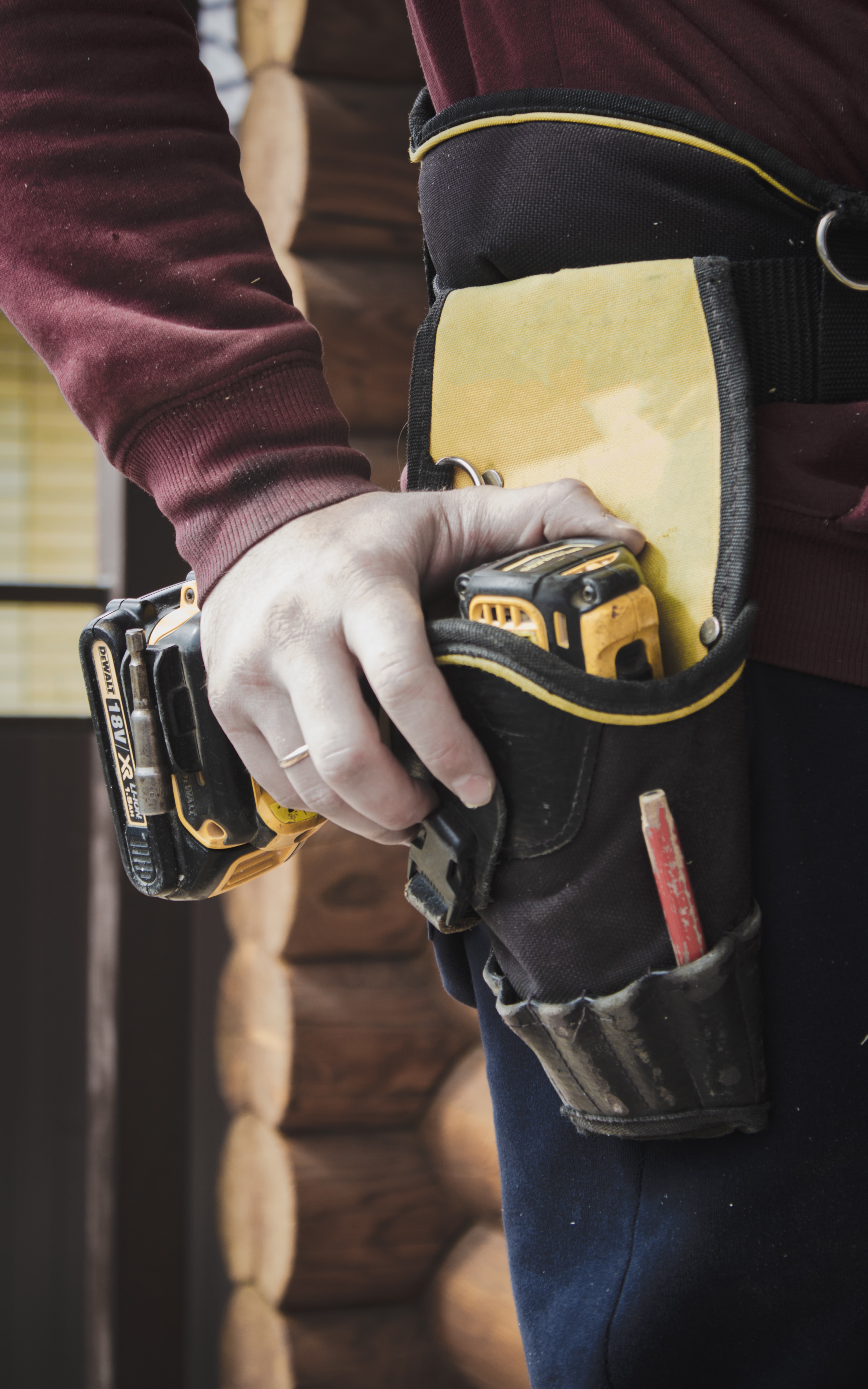 A builder's hand grabbing a drill that is sitting in their tool belt